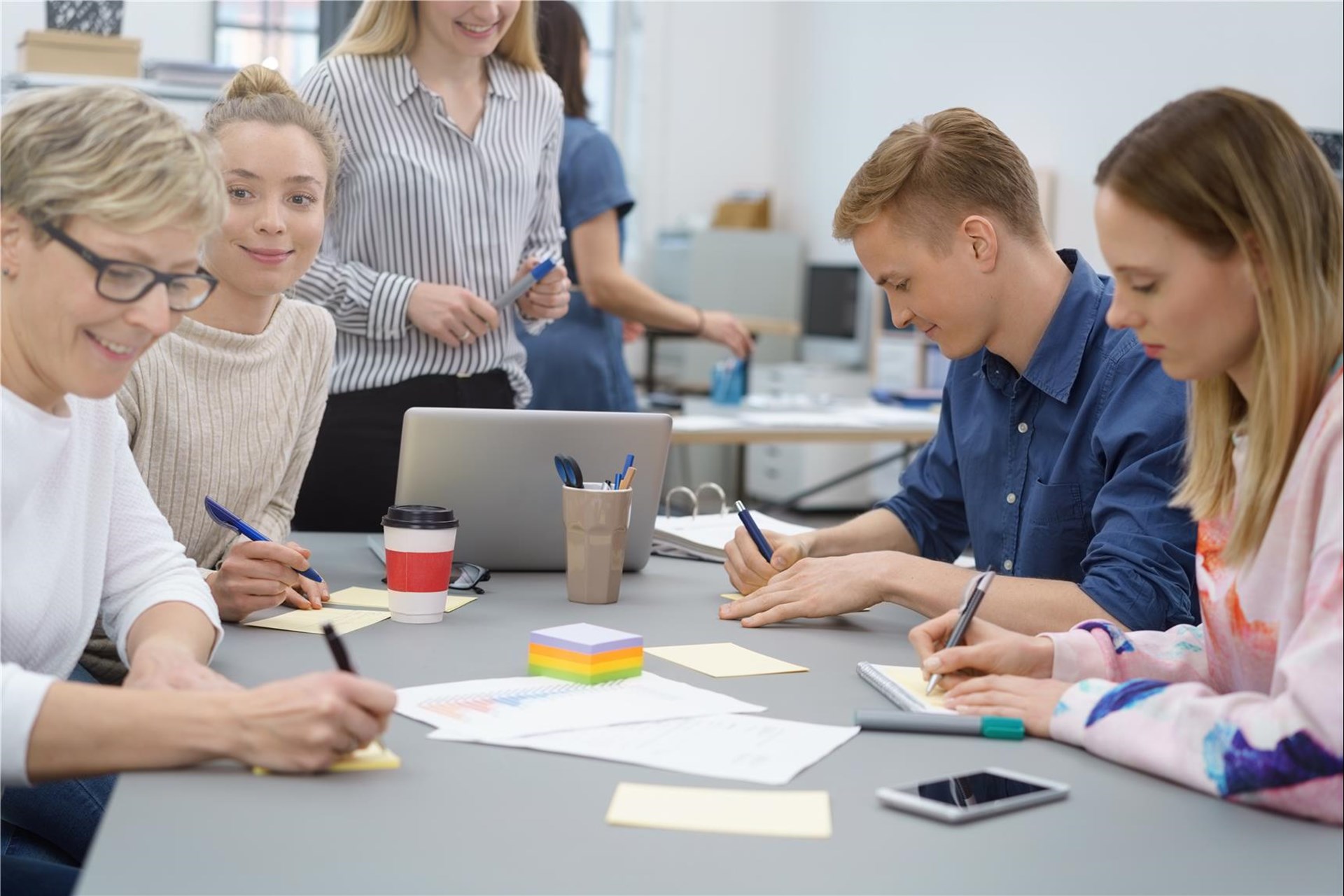 Vier Personen - drei Frauen und ein Mann - sitzen gemeinsam um einen Tisch und notieren etwas auf Post-Its. 
