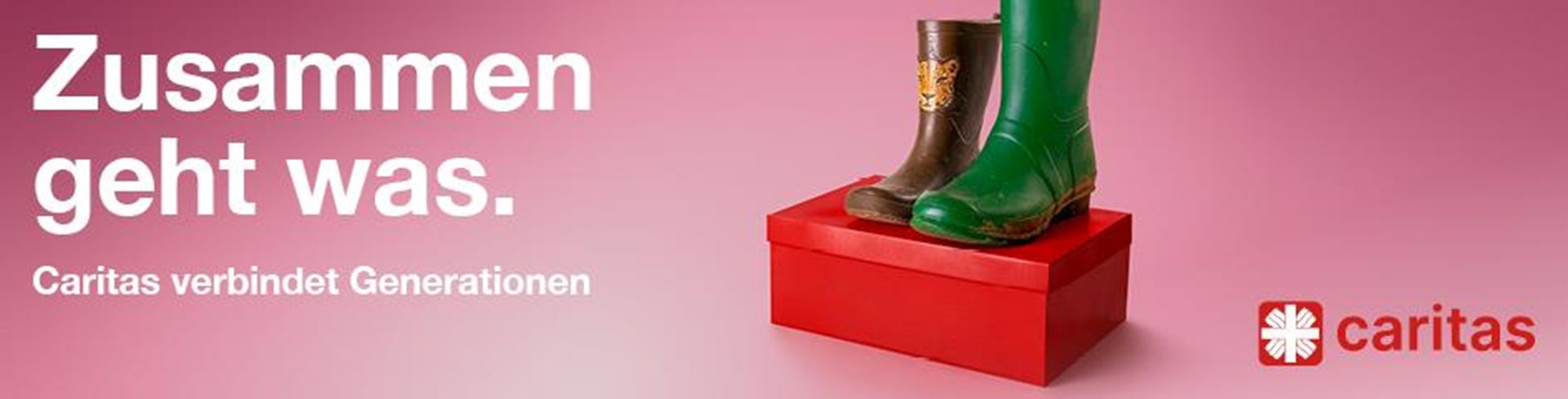 Auf einem roten Schuhkarton sind vor einem rosa Hintergrund ein Paar Gummistiefel zu sehen. Der linke Schuh ist ein brauner Kindergummistiefel mit einem Tigerkopf in kleiner Schuhgröße, der rechte ein hoher grüner Gummistiefel in großer Schuhgröße. Darüber steht das Kampagnenmotto: Zusammen geht was. Caritas verbindet Generationen.